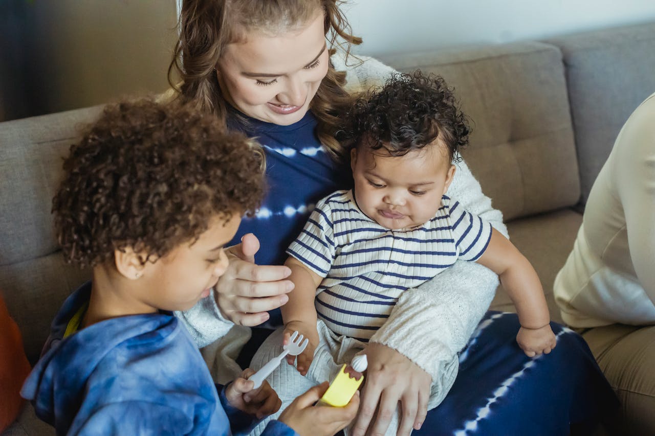 Mother cuddling baby and playing toys with son