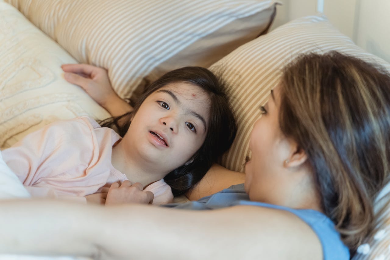 A Woman Embracing a Young Girl while Lying on the Bed