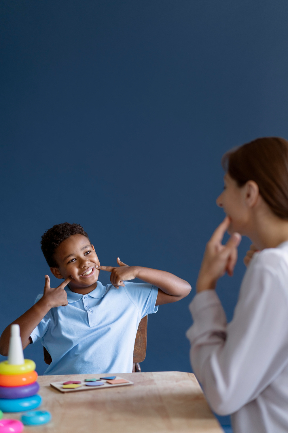 child smiling while pointing at own smile with therapist