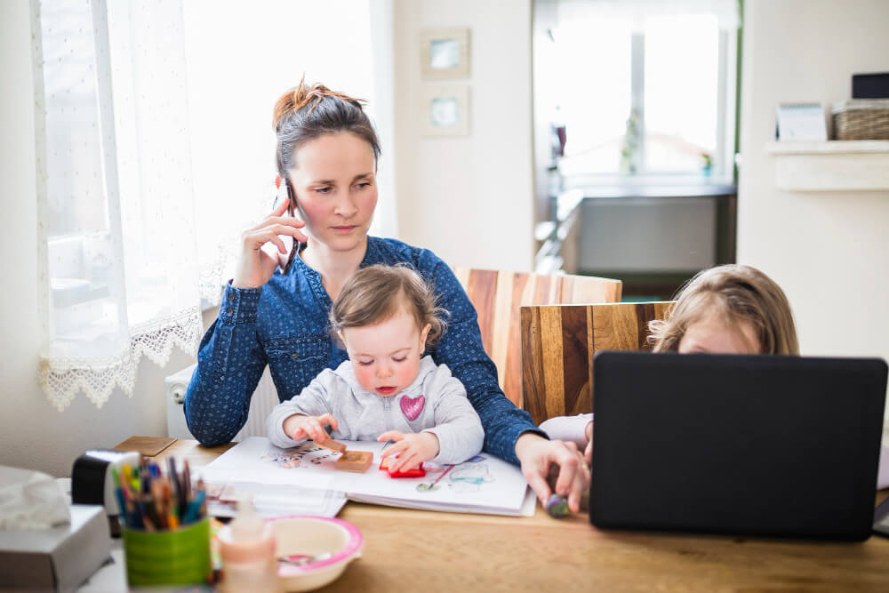 Mom with two kids on phone while older child looks at computer