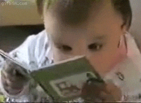 Baby reading a small green-covered book, holding it close and looking intently at the pages, with a curious expression.