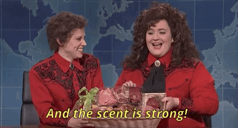 Two women in red outfits smile on a TV set, presenting gift baskets; caption reads, 'And the scent is strong!'