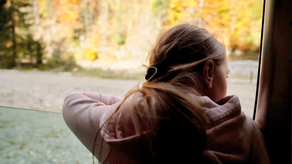 Girl looks out window, looking glum